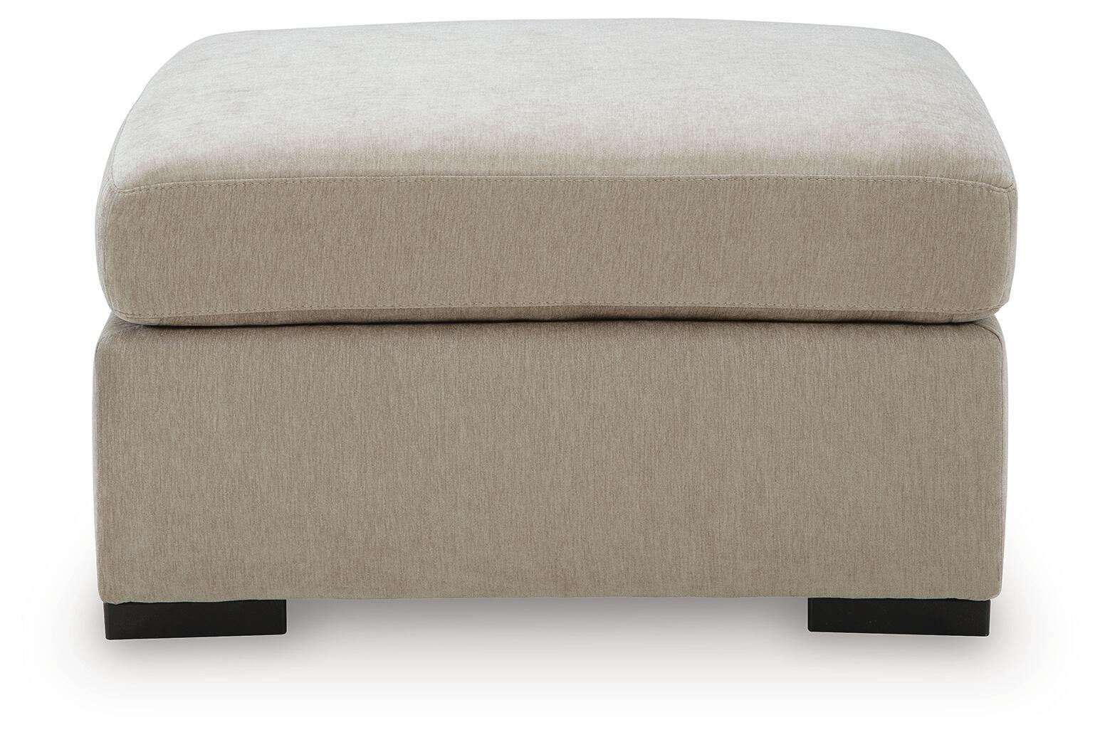 Oversized accent ottoman in light beige fabric with thick padded lid and dark block legs.