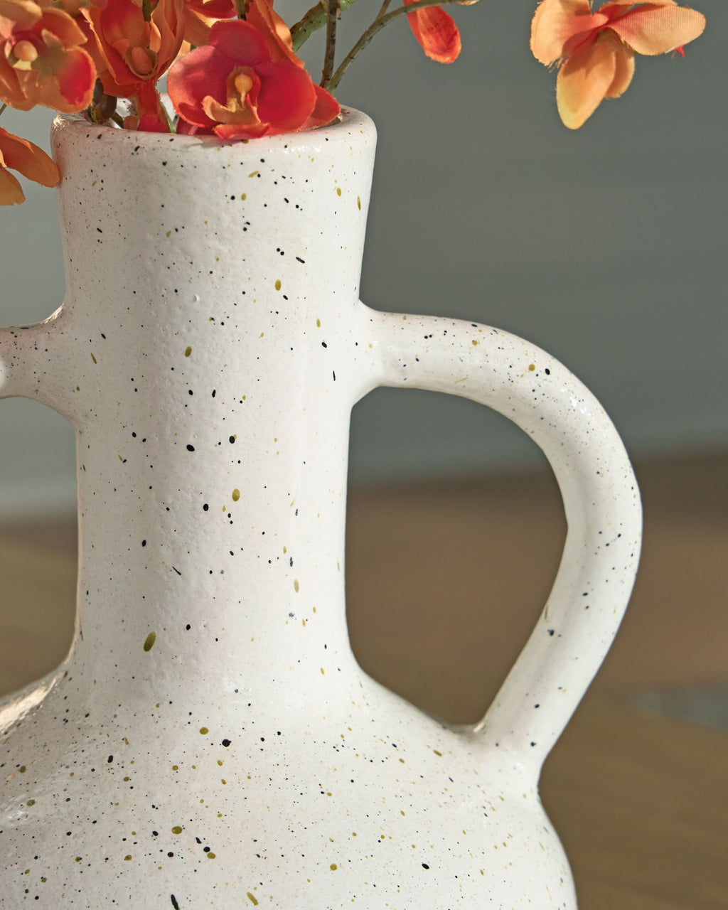 Speckled white ceramic vase with red flowers, showing one loop handle.