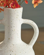 Speckled white ceramic vase with red flowers, showing one loop handle.