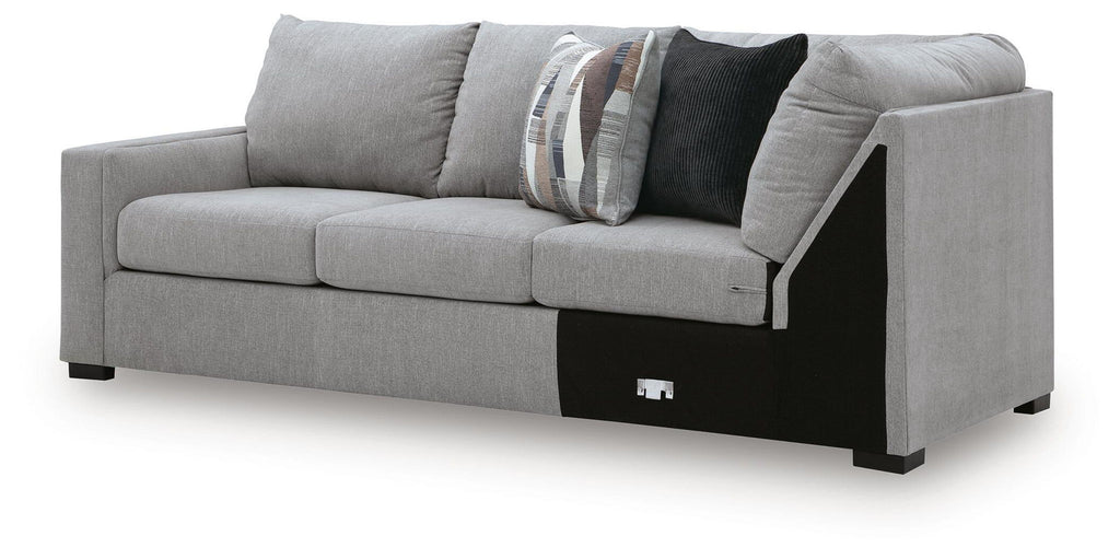Grey sectional sofa with corner wedge, black base trim and patterned throw pillows on back