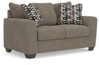 Grey suede loveseat with two patterned throw pillows and cushioned seat