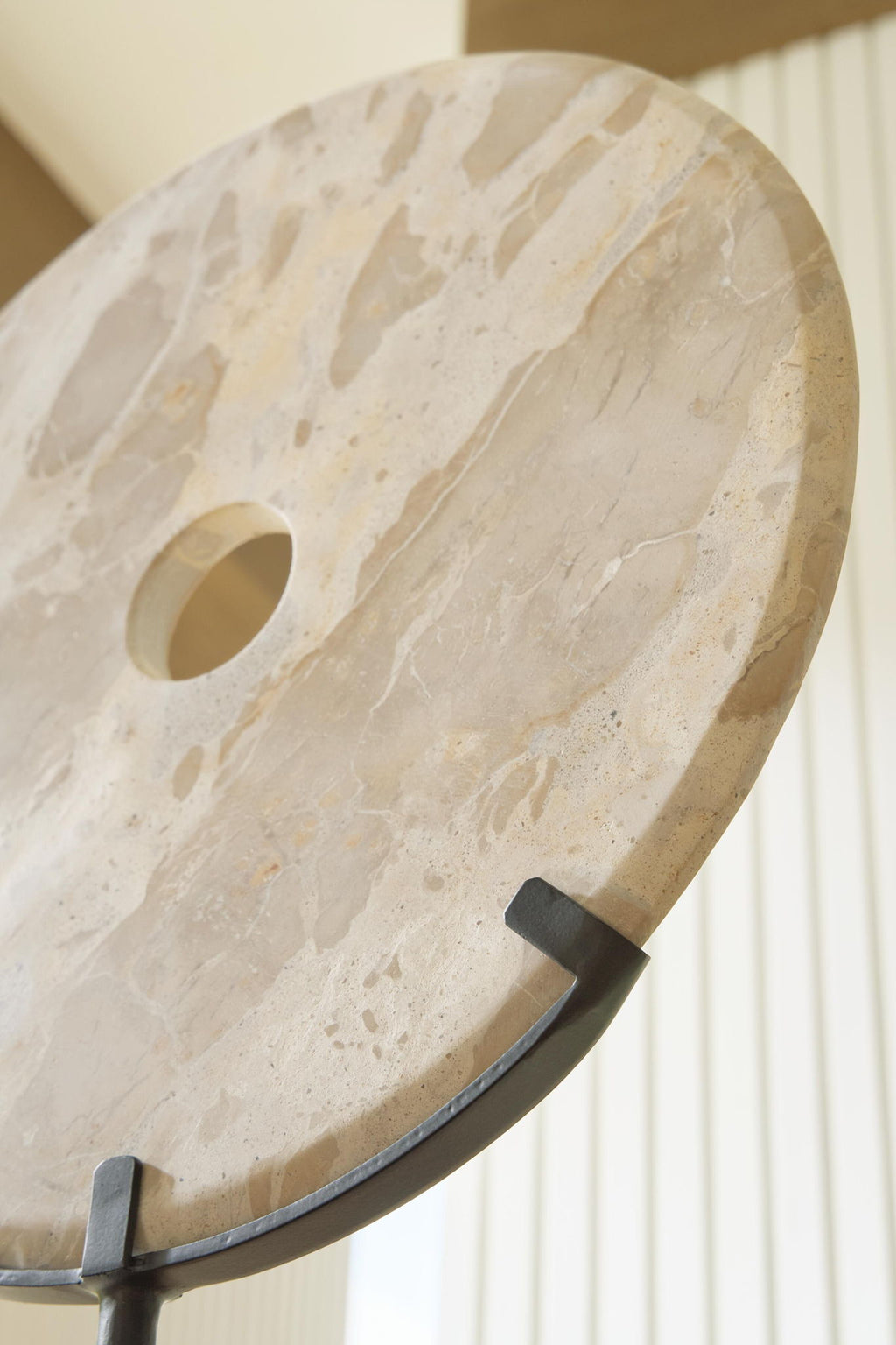 Close-up of light beige circular sculpture with side notch and drilled hole