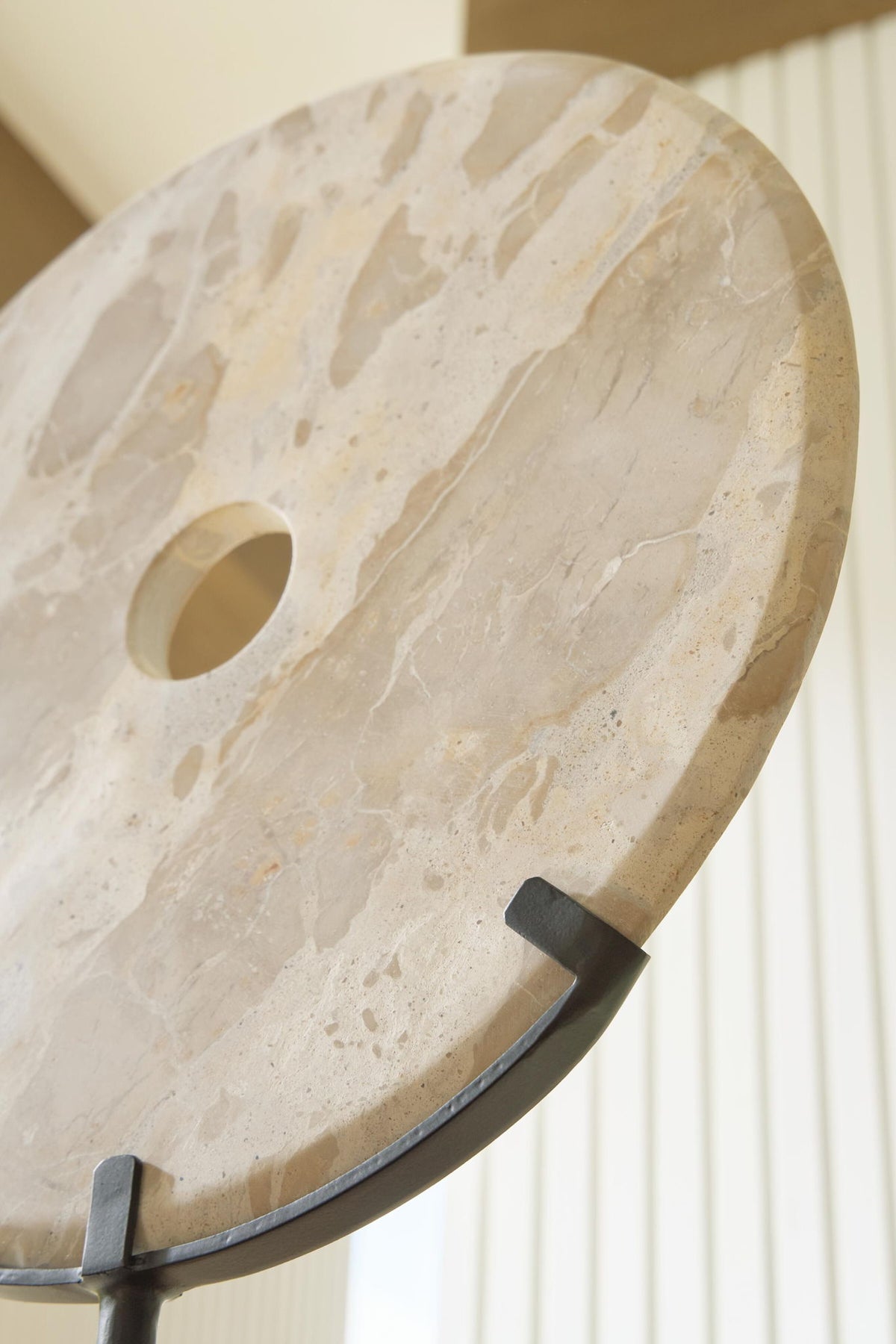 Close-up of light beige circular sculpture with side notch and drilled hole