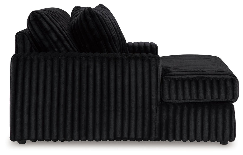 Oversized chaise with ribbed black fabric, curved arm and upholstered backrest.
