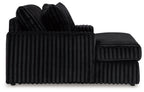 Oversized chaise with ribbed black fabric, curved arm and upholstered backrest.