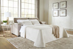 Light gray sofa sleeper with spread white bedding and stacked throw pillows
