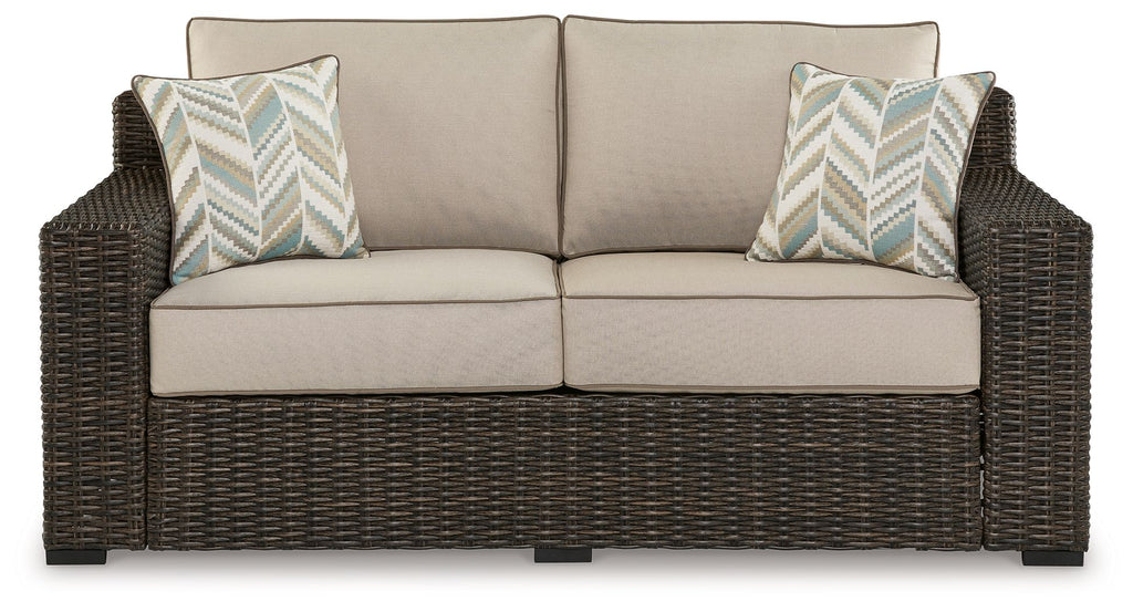 Brown wicker loveseat with beige cushions and two chevron throw pillows