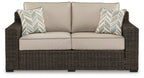Brown wicker loveseat with beige cushions and two chevron throw pillows