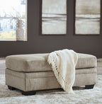 Upholstered ottoman in light beige with black legs and a folded throw on top.