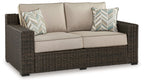 Brown wicker loveseat with beige cushions and two patterned throw pillows