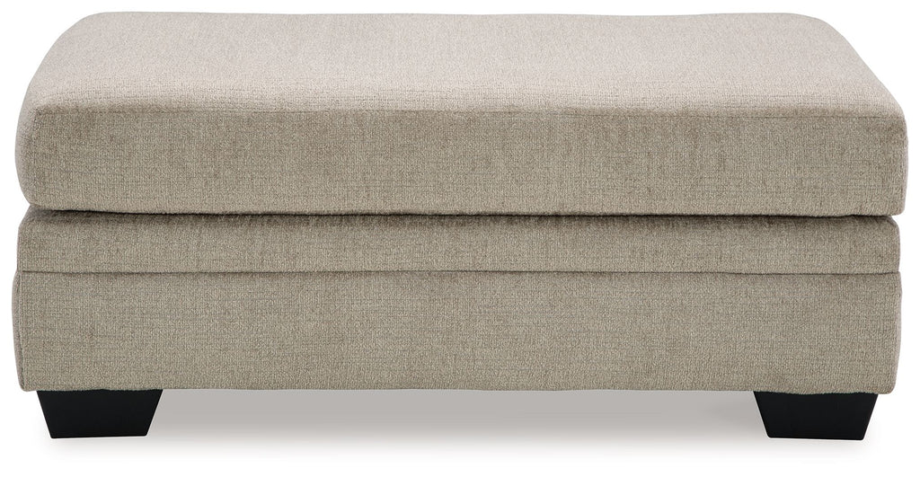 Upholstered ottoman with light beige fabric top, stacked base, black legs.