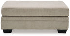 Upholstered ottoman with light beige fabric top, stacked base, black legs.