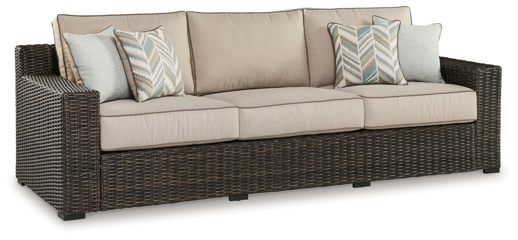 Brown wicker sofa with beige seat cushions and two patterned throw pillows