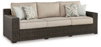 Brown wicker sofa with beige seat cushions and two patterned throw pillows