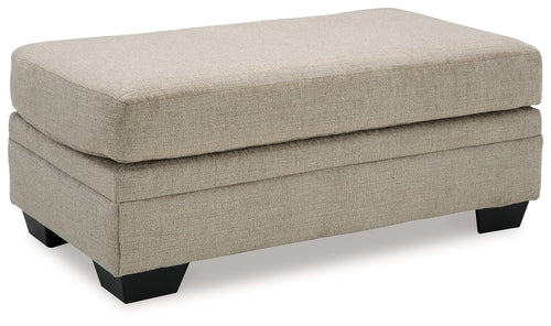 Upholstered ottoman with light beige top and base, black legs, square arms.