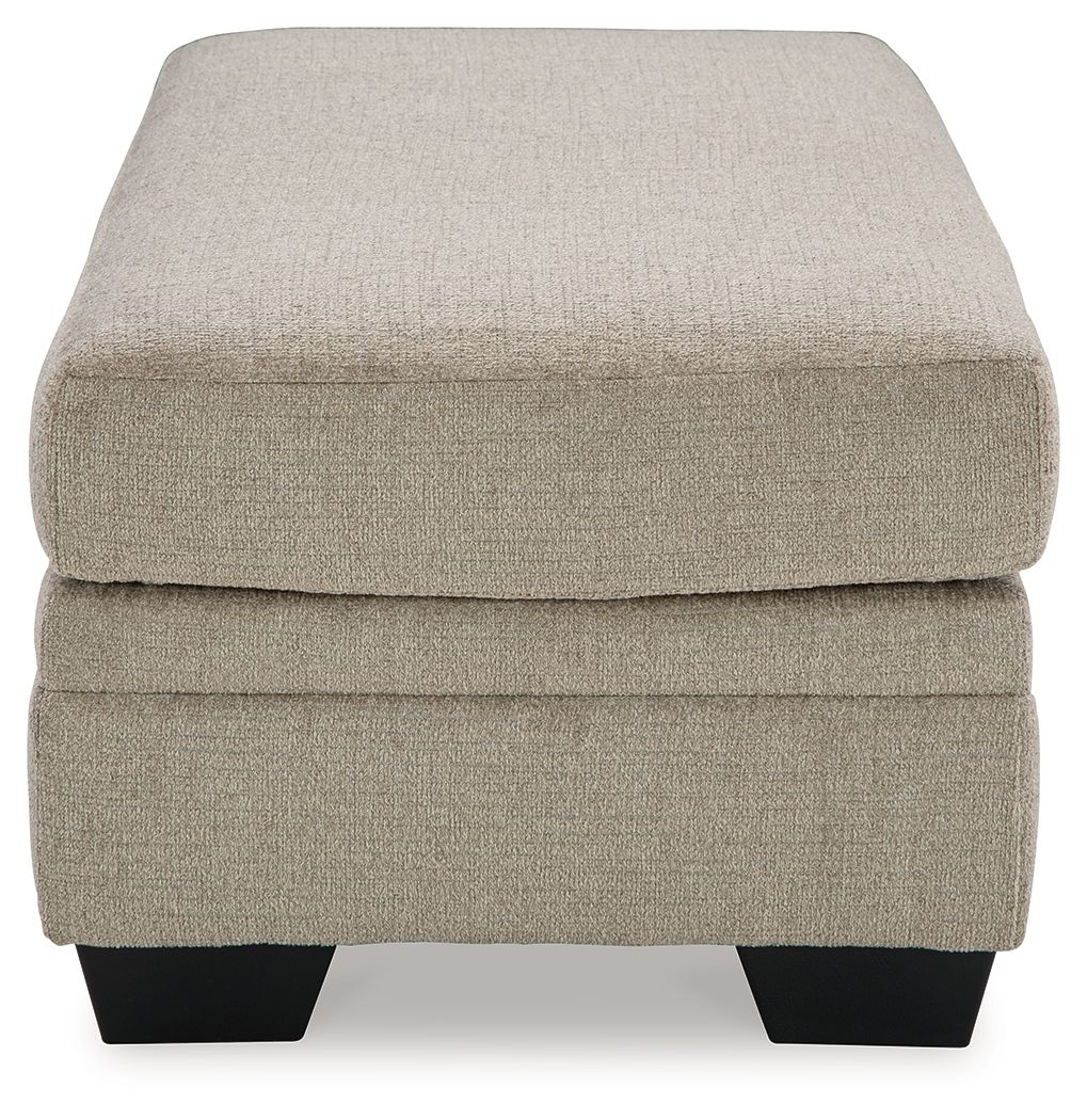 Upholstered ottoman in light beige with rounded corners and black legs.