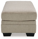 Upholstered ottoman in light beige with rounded corners and black legs.