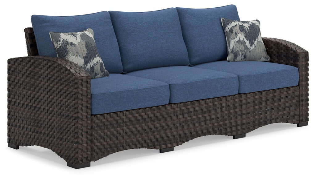 Outdoor sofa with blue cushions, brown wicker frame, two patterned throw pillows