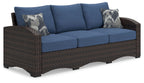Outdoor sofa with blue cushions, brown wicker frame, two patterned throw pillows