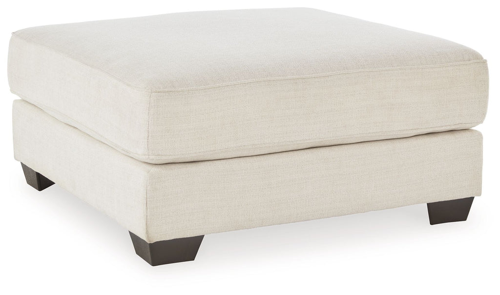 Oversized ottoman with beige fabric upholstery and dark tapered feet.