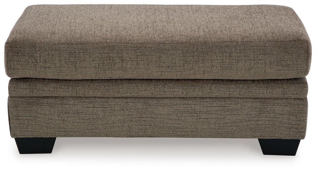 Upholstered ottoman in dark brown fabric with stitched panels and black legs.