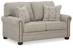 Light gray-beige loveseat with two patterned pillows and gold nail trim