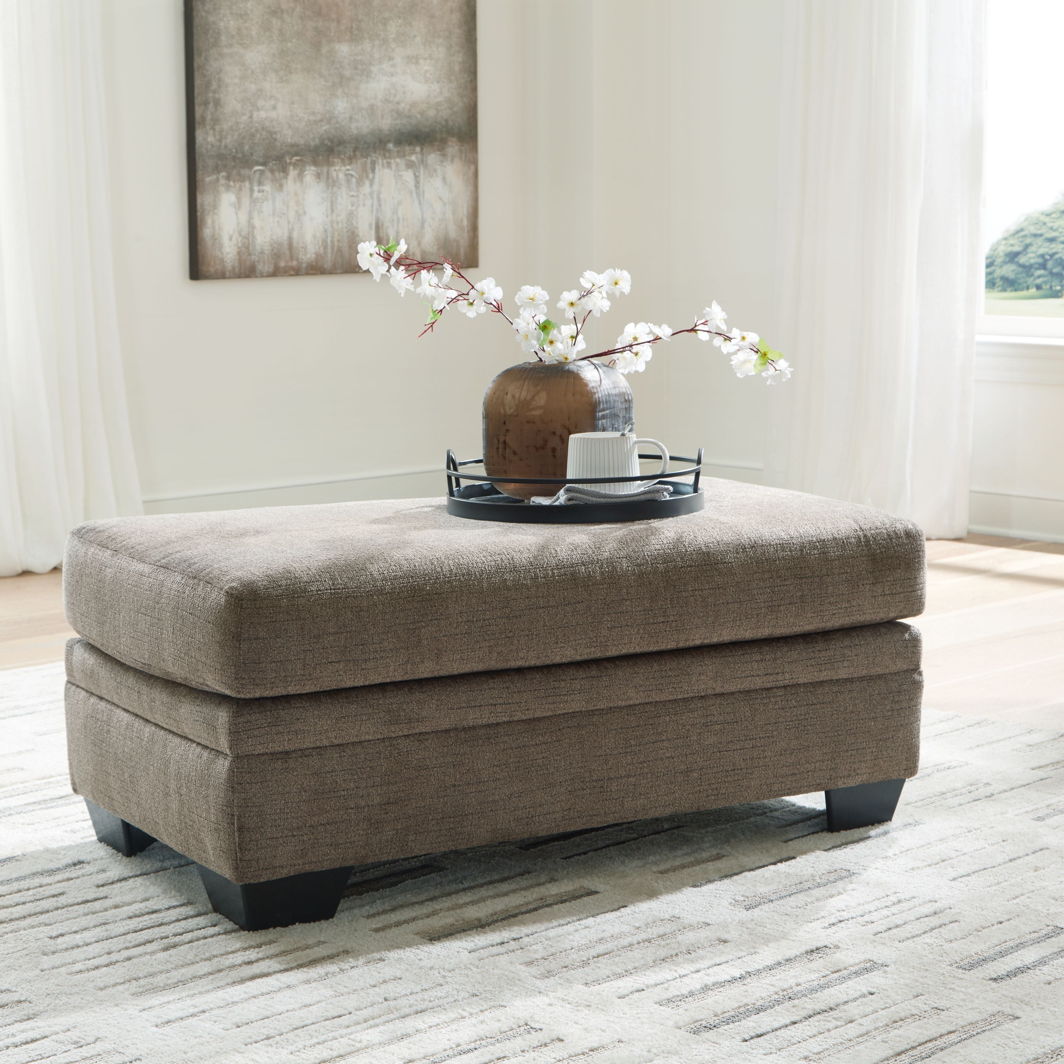 Upholstered ottoman in light brown fabric with black legs and a short display tray.
