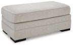 Light gray upholstered ottoman with rectangular top and stitched side panels